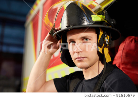 Portrait of a muscular, handsome firefighter on a fire truck background, holding a fire helmet Portrait of a muscular, handsome firefighter on a fire truck background, holding a fire helmet 91610679
