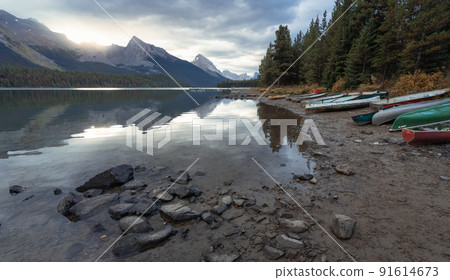 Empty boats on the shore of a lake during sunrise surrounded by mountains, Jasper N.Park, Canada 91614673