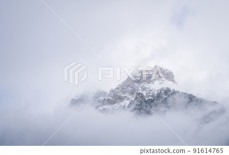 Isolated snowy alpine peak shrouded by clouds and fog, Yoho N. Park, Canada 91614765