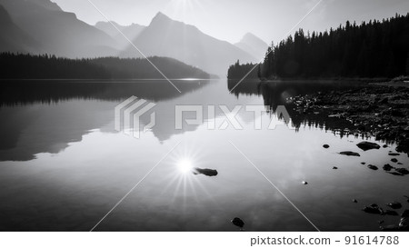 Sun reflecting in still alpine lake surrounded by mountains, monochromatic, Jasper NP, Canada 91614788