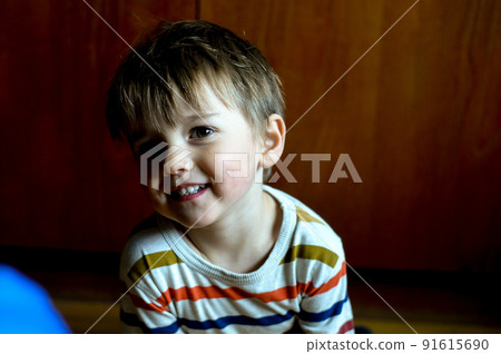 Face of nice baby child. Portrait of happy joyful laughing beautiful little boy smiling. Funny kid playing while sitting on wooden floor in the room. 91615690