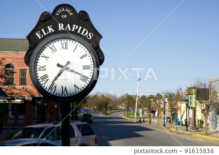 ELK RAPIDS, MICHIGAN, UNITED STATES - MAY 16, 2018: Main street in the small American town of Elk Rapids in northern Michigan with old longcase clock ELK RAPIDS, MICHIGAN, UNITED STATES - MAY 16, 2018: Main street in the small American town of Elk Rapids in northern Michigan with old longcase clock 91615838