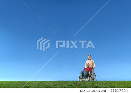A middle-aged woman who takes care of an elderly woman in a wheelchair against the background of the blue sky. Old age, second life, old age, long-term care image A middle-aged woman who takes care of an elderly woman in a wheelchair against the background of the blue sky. Old age, second life, old age, long-term care image 91617464
