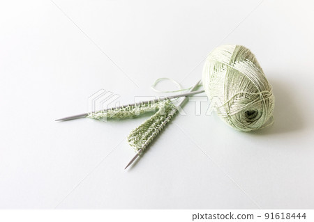 Green yarn thread with knitting needles on a green background for knitting. 91618444