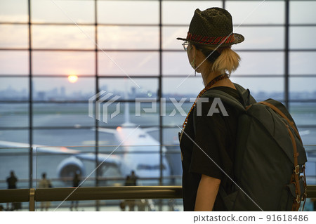 asian woman air traveler looking at sunrise through window while walking in airport terminal building asian woman air traveler looking at sunrise through window while walking in airport terminal building 91618486