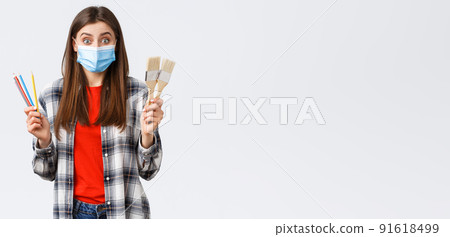 Social distancing, leisure and hobbies on covid-19 outbreak, coronavirus concept. Excited cheerful girlfriend suggest drawing together, holding painting brushes and colored pencils, wear medical mask 91618499