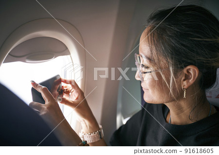asian woman passenger taking a photo with cellphone through airplane window 91618605