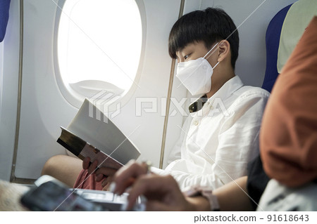 fifteen year old boy on airplane wearing face mask reading a book fifteen year old boy on airplane wearing face mask reading a book 91618643