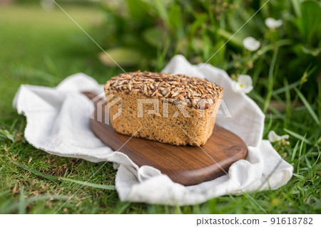 homemade grey bread with seeds on the wood board with the white cloth napkin on the green grass. High quality photo 91618782