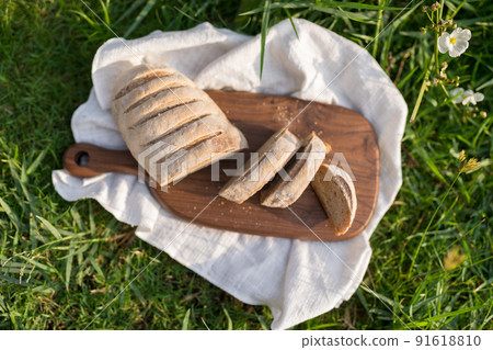 Composition of homemade white flour bread on wood board with white cloth napkin on the green grass . High quality photo Composition of homemade white flour bread on wood board with white cloth napkin on the green grass . High quality photo 91618810