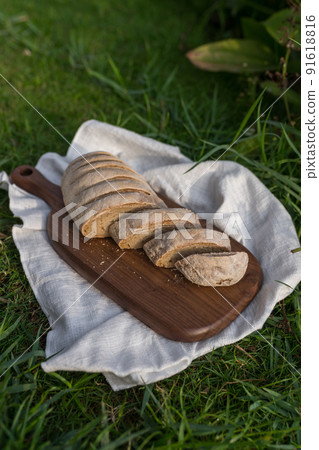 Composition of homemade white flour bread on wood board with white cloth napkin on the green grass . High quality photo 91618816