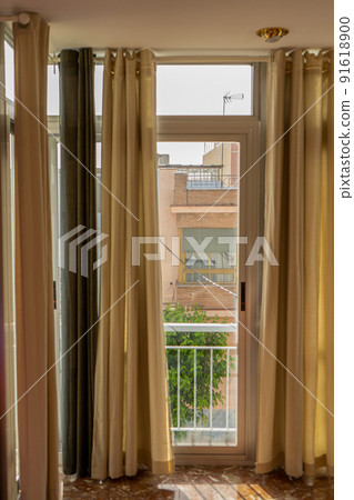 Vertical view of a living room with some old cream-colored curtains protecting it from the sun behind the window that acts as a wall 91618900