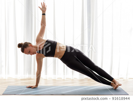 Young woman doing her morning yoga routine at home near the big window 91618944