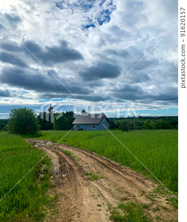 Country road along green fields leading to house. Blue sky white clouds natural landscape background Country road along green fields leading to house. Blue sky white clouds natural landscape background 91620157