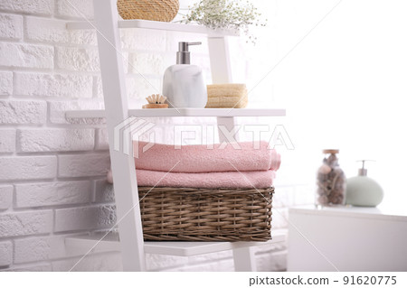 Basket with clean towels on shelving unit in bathroom 91620775
