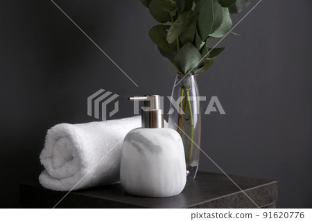 Clean soft towel and soap dispenser on stand near black wall Clean soft towel and soap dispenser on stand near black wall 91620776