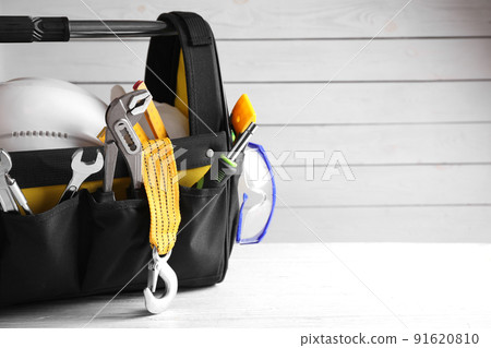 Black bag with construction tools on white wooden table. Space for text Black bag with construction tools on white wooden table. Space for text 91620810