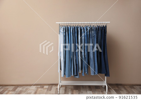Rack with stylish jeans on near beige wall Rack with stylish jeans on near beige wall 91621535