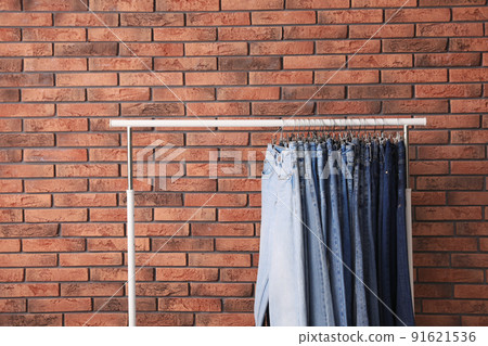 Rack with stylish jeans near brick wall Rack with stylish jeans near brick wall 91621536