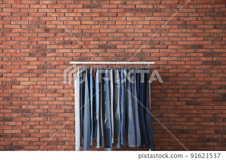 Rack with stylish jeans near brick wall Rack with stylish jeans near brick wall 91621537