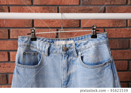 Rack with stylish jeans near brick wall, closeup Rack with stylish jeans near brick wall, closeup 91621539