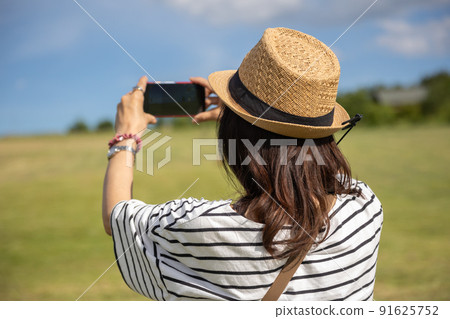 A woman taking a picture of a summer plateau landscape with a smartphone 91625752