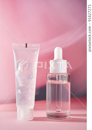 A transparent bottle of cosmetic gel and a bottle of serum on a pink background. 91627271