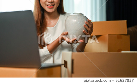 Woman online shop owner packing her goods into a cardboard box. Pottery online selling Woman online shop owner packing her goods into a cardboard box. Pottery online selling 91627837