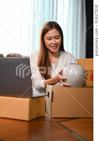 Woman online shop owner packing her goods into a cardboard box. 91627838
