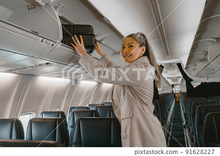 Asian Woman traveler putting luggage into overhead locker on airplane during boarding Asian Woman traveler putting luggage into overhead locker on airplane during boarding 91628227