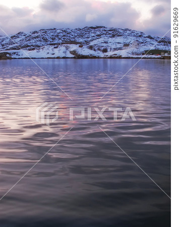 Copyspace of a calm sunset north of the Polar Circle on a calm winters day. Quiet Portage Lake with snow capped mountains on a cold winter day. An iced rural landscape in subzero temperature 91629669