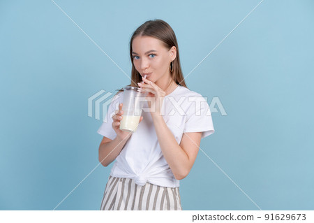 Cute caucasian young girl in white t-shirt and striped pants drinks milkshake 91629673