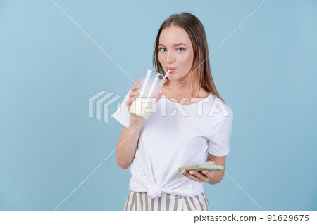 Girl stands with cocktails and smartphone on copy blue background in studio 91629675