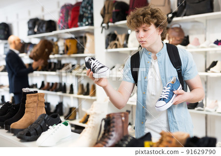 Interested teenager choosing canvas sneakers for sports and hiking in store 91629790