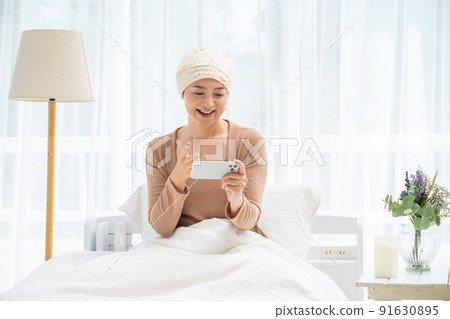 一位戴著醫用帽子的中年婦女在床上看著她的智能手機 91630895