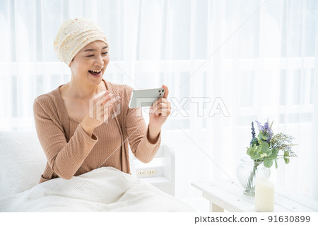 一位戴著醫用帽子的中年婦女在床上看著她的智能手機 91630899