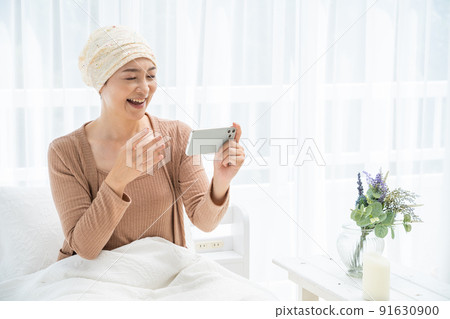 一位戴著醫用帽子的中年婦女在床上看著她的智能手機 91630900