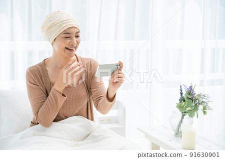 一位戴著醫用帽子的中年婦女在床上看著她的智能手機 91630901