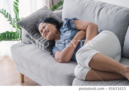 Woman suffering from stomachache lying down on the sofa at home. abdominal pain, Gastritis, Period, menstruation. Woman suffering from stomachache lying down on the sofa at home. abdominal pain, Gastritis, Period, menstruation. 91631615