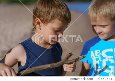 cute caucasian boys looking at a ladybug sitting on wood stick. summer evening on beach 91632574