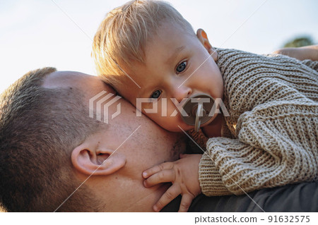 little baby boy on his dad's hands, sucking a pacifier. Spending time outdoors together. Father's day little baby boy on his dad's hands, sucking a pacifier. Spending time outdoors together. Father's day 91632575