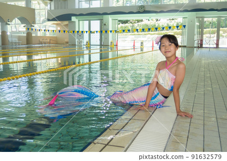 一個可愛的小學女孩在溫水游泳池裡練習美人魚 91632579