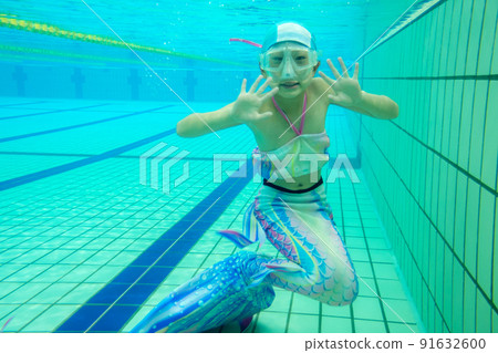 Underwater photo of an elementary school girl practicing mermaid in a heated pool 91632600