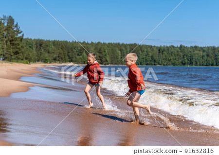 cute caucasian boys wearing red hoodies and blue underpants running from waves in Ladoga lake with enthusiasm cute caucasian boys wearing red hoodies and blue underpants running from waves in Ladoga lake with enthusiasm 91632816