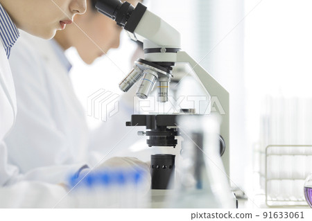 A woman in a white coat looking through a microscope 91633061
