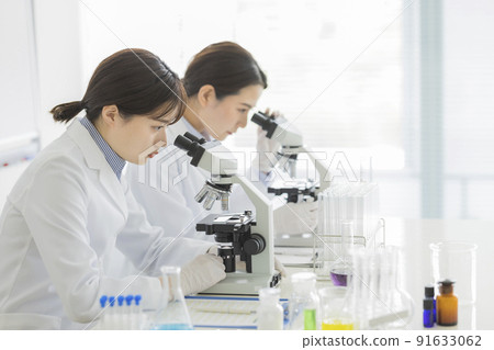 A woman in a white coat looking through a microscope A woman in a white coat looking through a microscope 91633062