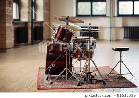 Horizontal image of drum kit for drummer standing on carpet at big empty studio 91633389