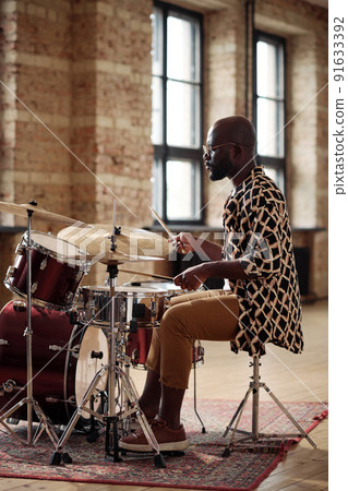 African man sitting at drums set and enjoying to play drums during his leisure activity African man sitting at drums set and enjoying to play drums during his leisure activity 91633392