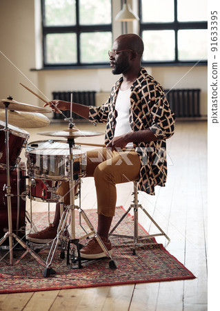 African drummer concentrating on his play on drums in a big empty studio African drummer concentrating on his play on drums in a big empty studio 91633395