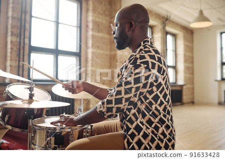 Young African drummer playing at drums set during rehearsal at musical studio Young African drummer playing at drums set during rehearsal at musical studio 91633428